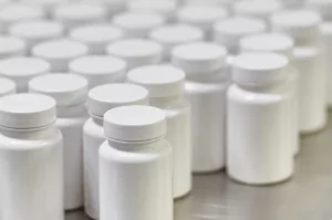 Rows of white plastic bottles with white caps arranged closely together on a flat surface. The bottles are uniform in size and shape, suggesting a mass production setting.